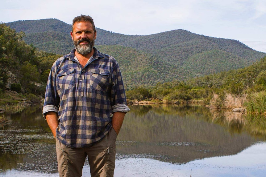 Wiradjuri man, Richard Swain standing in front a river and hills