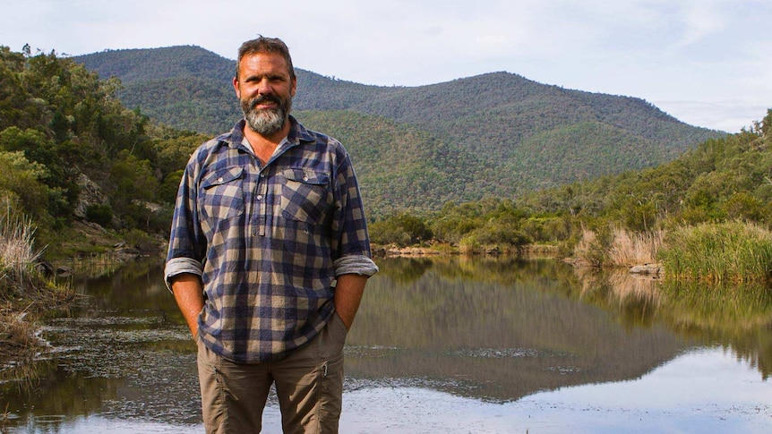 Wiradjuri man, Richard Swain standing in front a river and hills