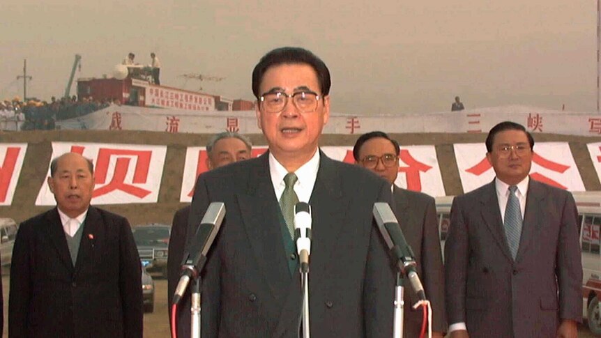 An old photo shows Li Peng behind three microphones on a red-carpet ceremony with a row of five male officials behind him.