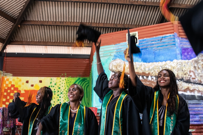 A group of indigenous students throw hats in the air and laugh.