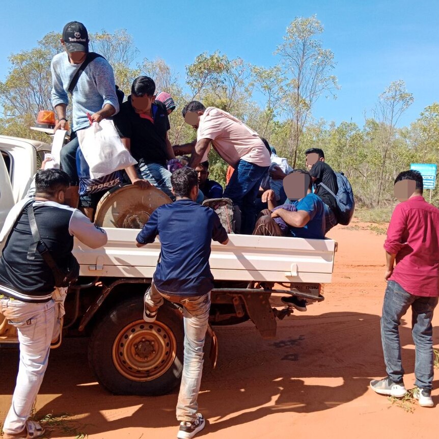 A group of men, their faces pixellated, climb aboard a ute on a dustry red outback road
