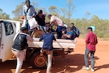 A group of men, their faces pixellated, climb aboard a ute on a dustry red outback road