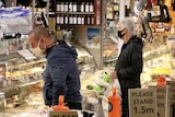 Two shoppers in masks wait at the counter of a deli at South Melbourne Market