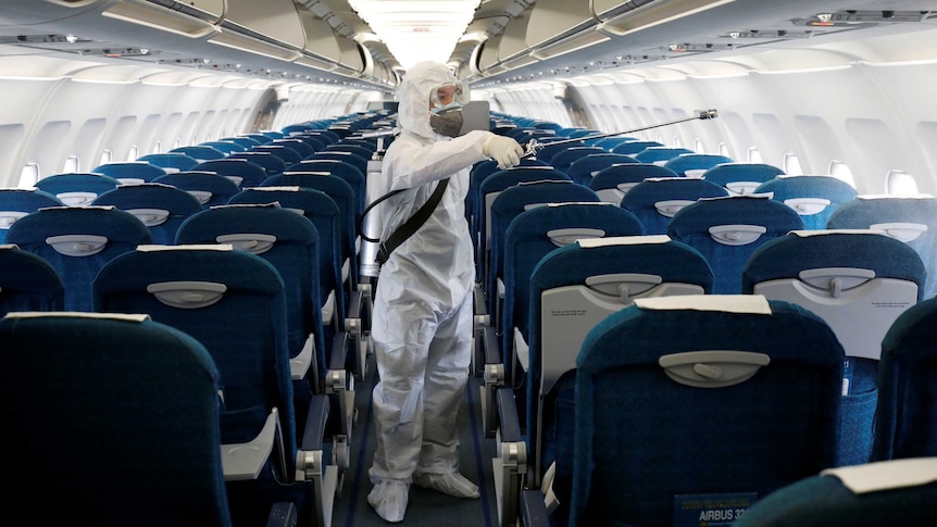 A man in hazmat gear sprays disinfectant on the cabin of a plane