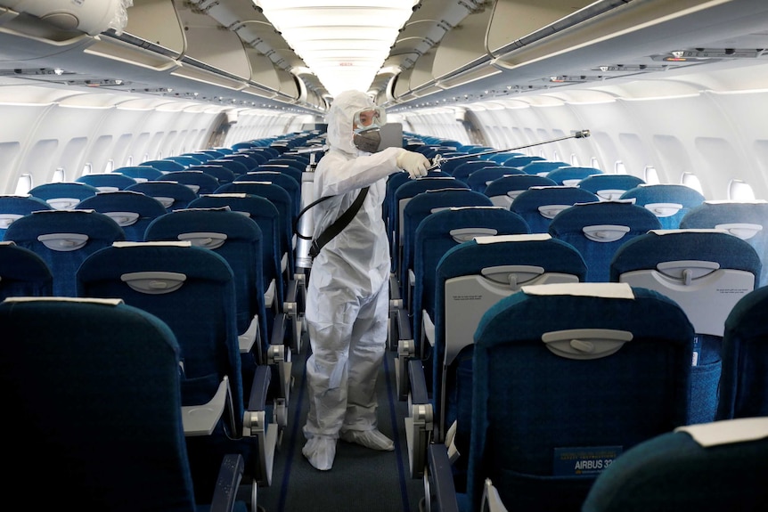 A man in hazmat gear sprays disinfectant in the cabin of a plane.
