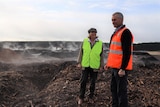 A man and woman wearing high-vis vests stand in mulch