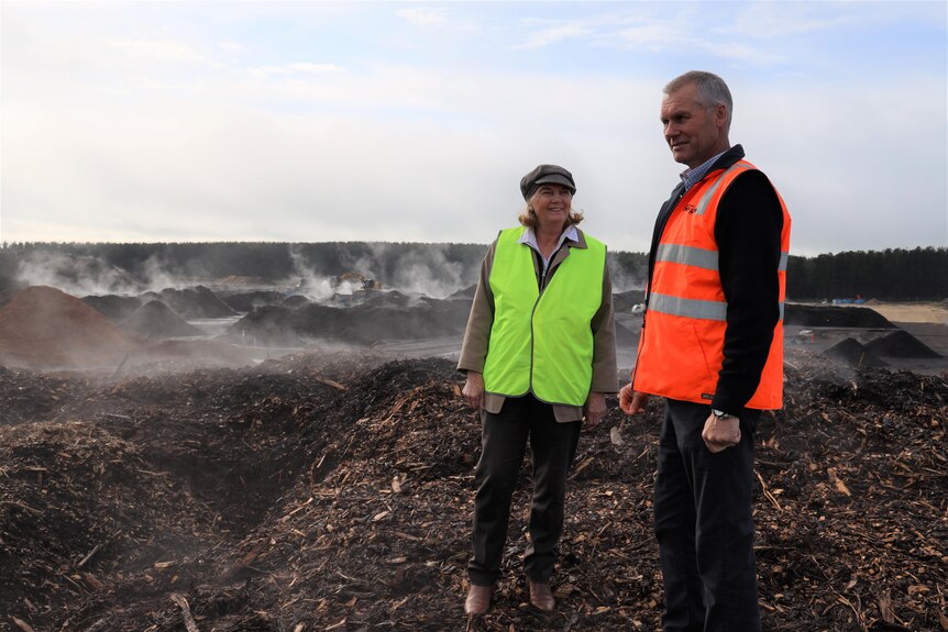 A man and woman wearing high-vis vests stand in mulch