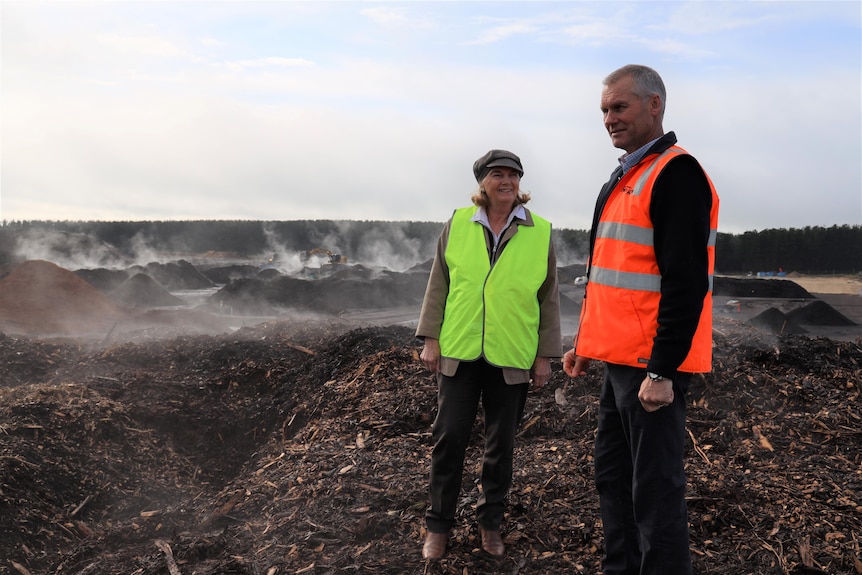 A man and woman wearing high-vis vests stand in mulch