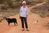 A woman stands in the red dirt of the outback with two dogs.