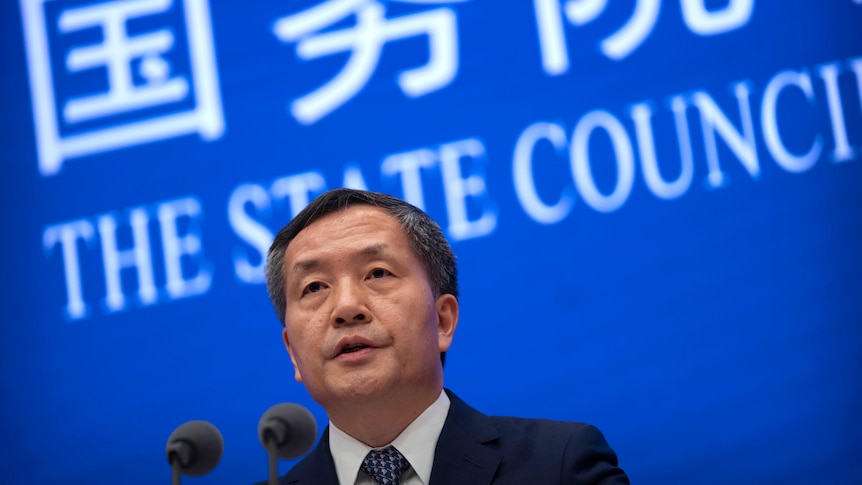 A Chinese man in front of a blue screen with chinese writing on it and "the state council" 