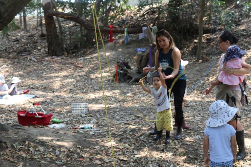 Parents standing around and playing with  children using ropes in a bush clearing