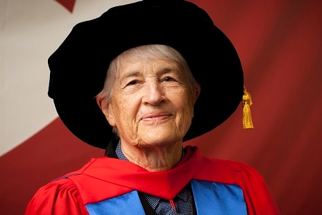 A woman in academic attire smiles at the camera