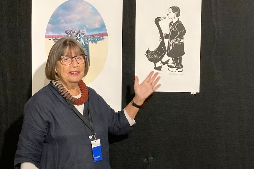 A woman stands in front of art on the wall. 