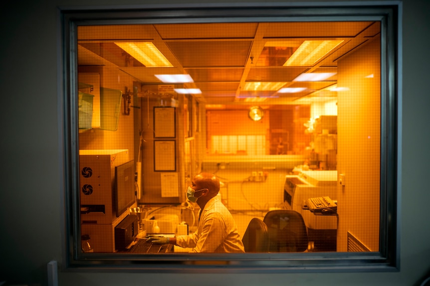 A man in a lab coat and face mask sits in a lab