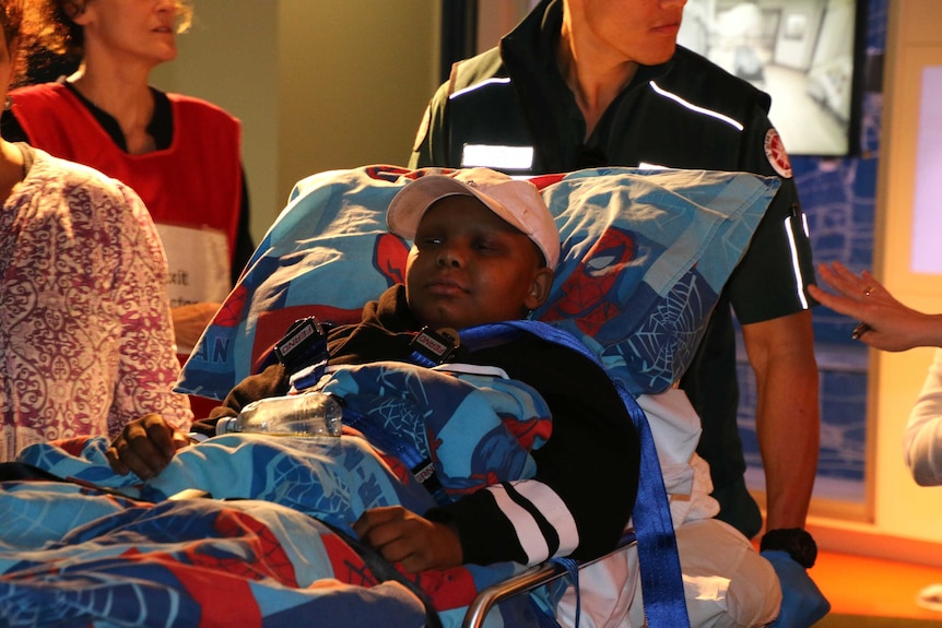 12-year-old Darius Eldouma lies on a stretcher with Spiderman sheets as it is pulled by a St John Ambulance paramedic.