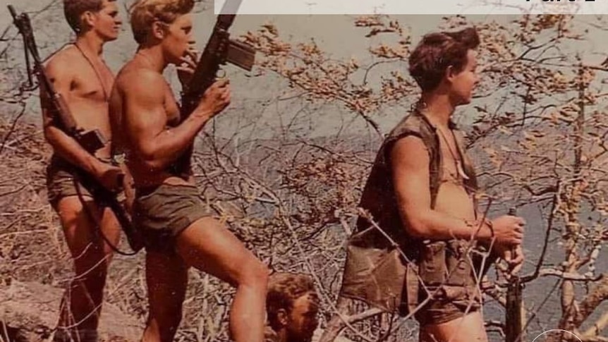 Four shirtless men with weapons in a rural setting.