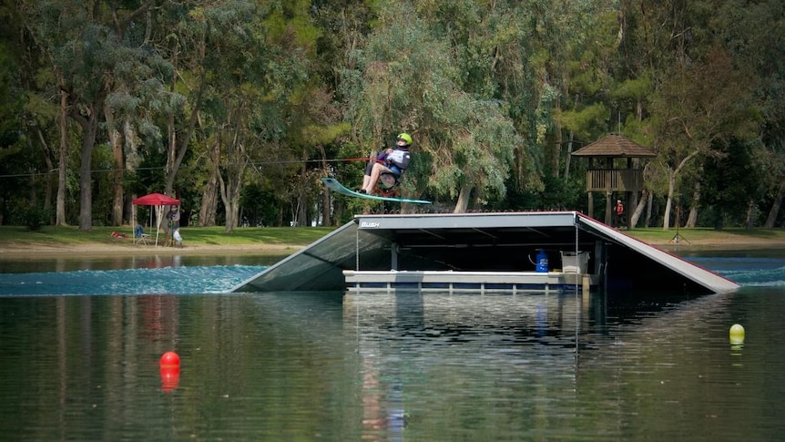 A women on a seated jetski is flying through the air just having left the ski jump.
