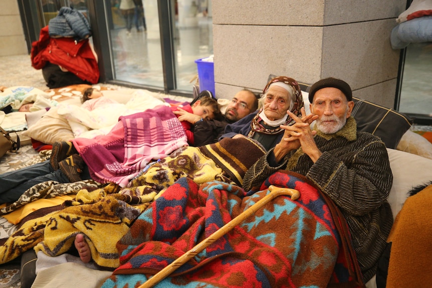 Three adults an a child lay down covered in colourful blankets. 