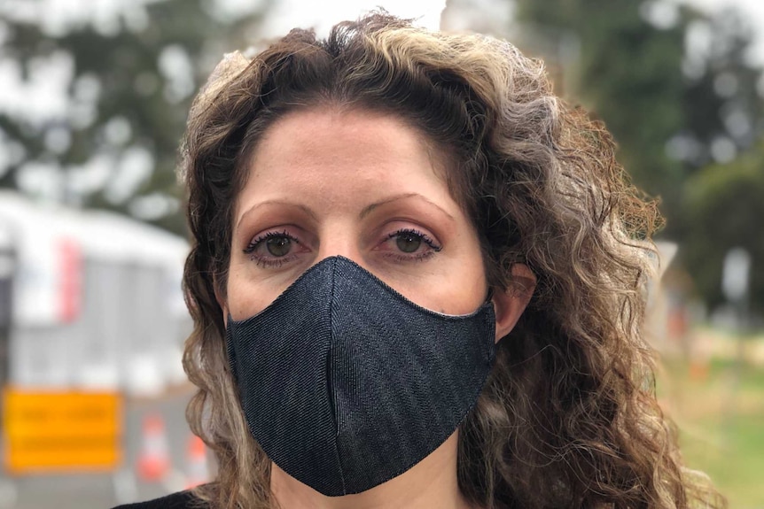 A portrait of a woman with long curly hair wearing a black mask and black top.