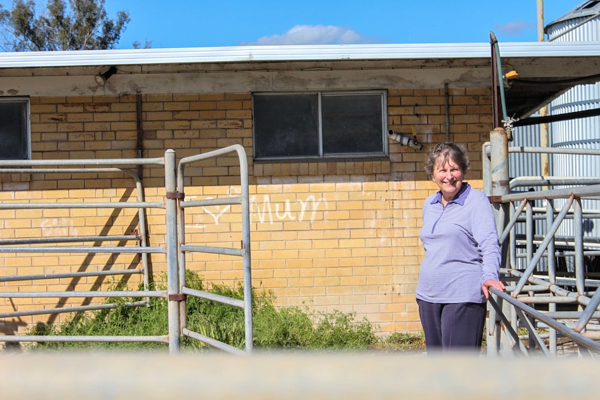 An older woman stands against a steel gate in front of a brick building.