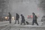 Four people cross a street during heavy snow. 