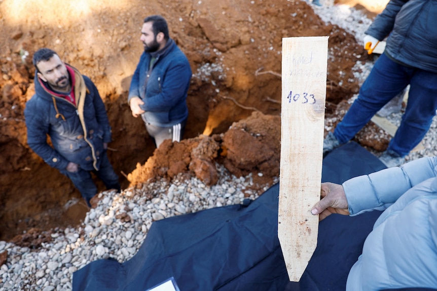 A man writes numbers on pieces of wood to prepare graves for victims of the deadly earthquake.