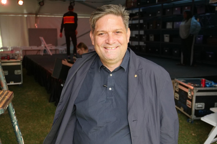 An Indigenous man in stands in the doorway of a large tent. Behind him, a stage is being set up.