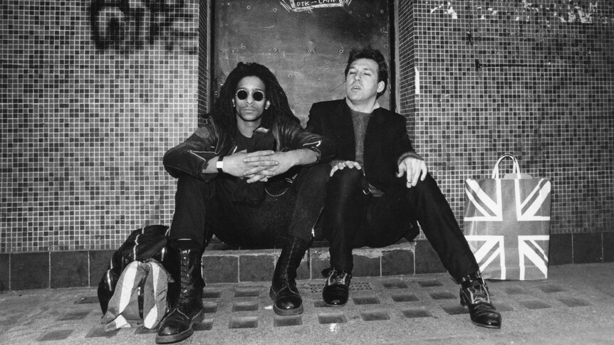 Black-and-white photo of two men sitting outside The Roxy nightclub in London.