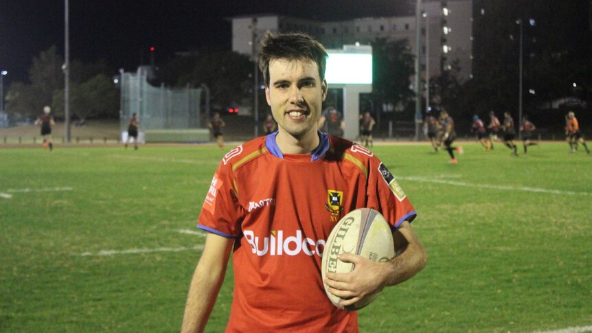 Connor stands facing the camera holding a rugby ball.