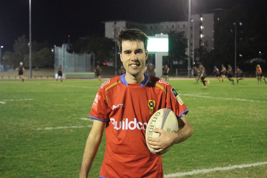 Connor stands facing the camera holding a rugby ball.