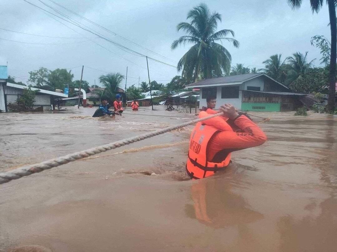 Someone in a life jacket drags two ropes behind him in waist-deep flood waters.