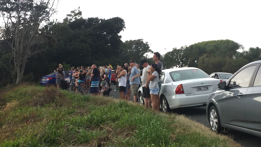 A group of people stand on a hill and look towards the beach where emergency services search for a missing boy.