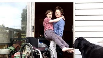 Woman holds teenage boy in arms, wheelchair in foreground