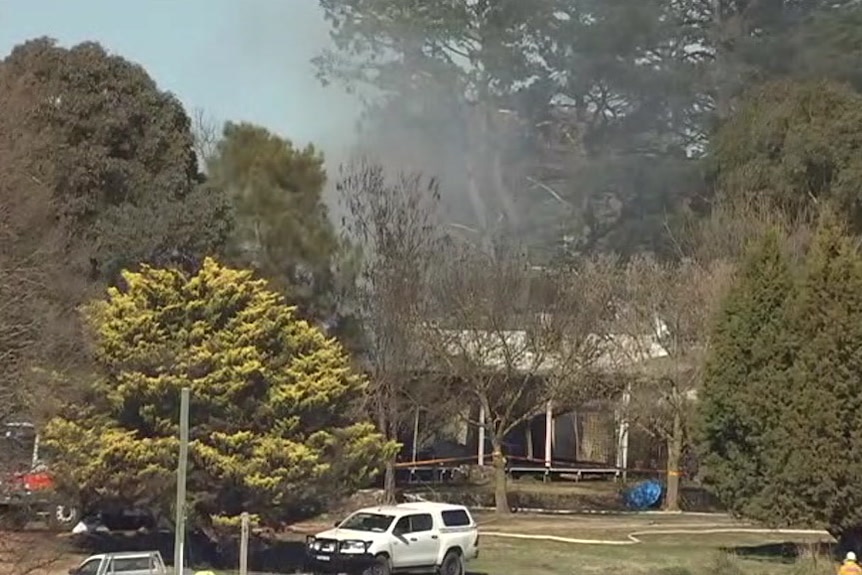 Cars in front of a burnt-out property with emergency tape around it.