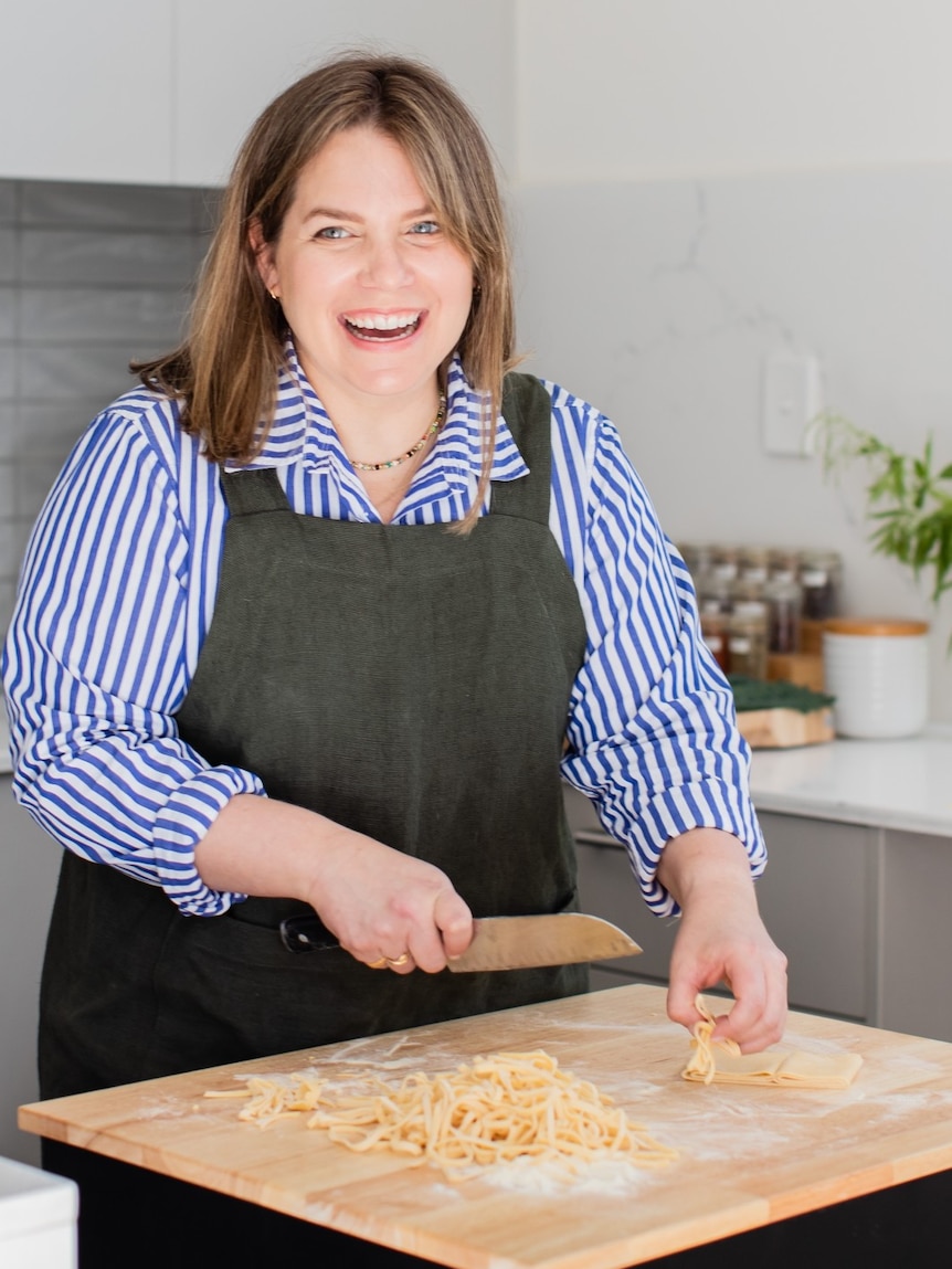 Danielle Alvarez wearing a stripy shirt and dark apron, laughing and chopping slices of fresh pasta.