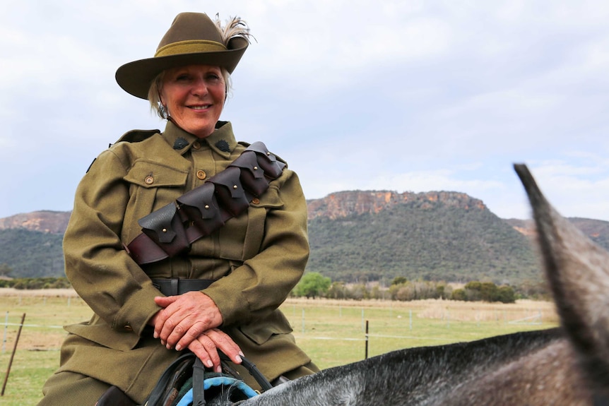 A woman dressed in military uniform sits atop a horse.