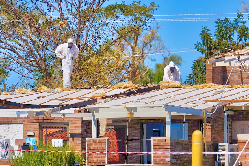 Two men in white coveralls stand on a roof which is being repaired
