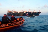 You look at coast guard personnel on small rubber boats approaching a cluster of large fishing ships.