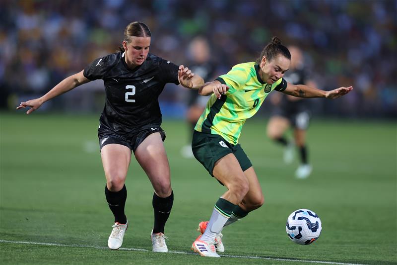 A atacante do Matildas, Caitlin Foord, se prepara e olha para baixo enquanto protege a bola de um zagueiro neozelandês. 