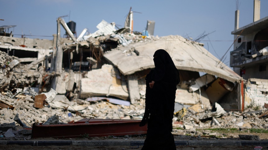 A Palestinian woman walks near the rubble of a house destroyed in an Israeli strike.