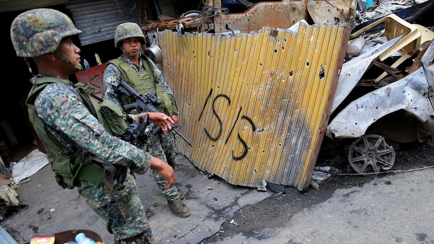 Two Philippines soldiers stand guard by a section of fence with "ISIS" painted on it.