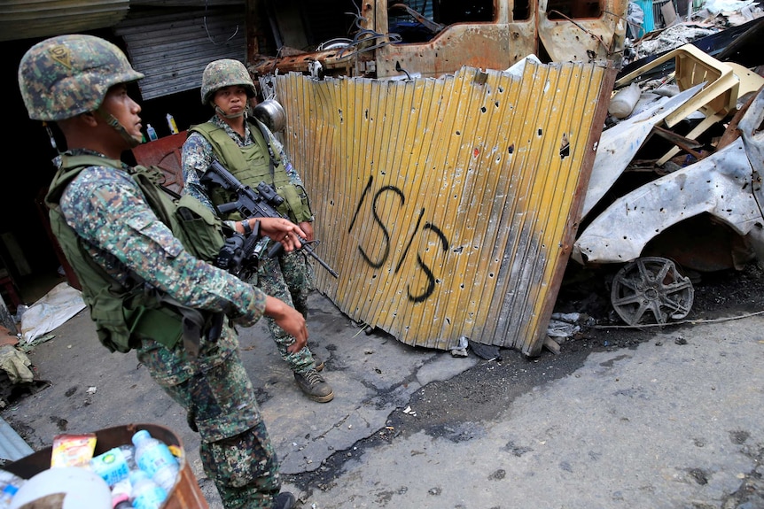 Two Philippines soldiers stand guard by a section of fence with "ISIS" painted on it.