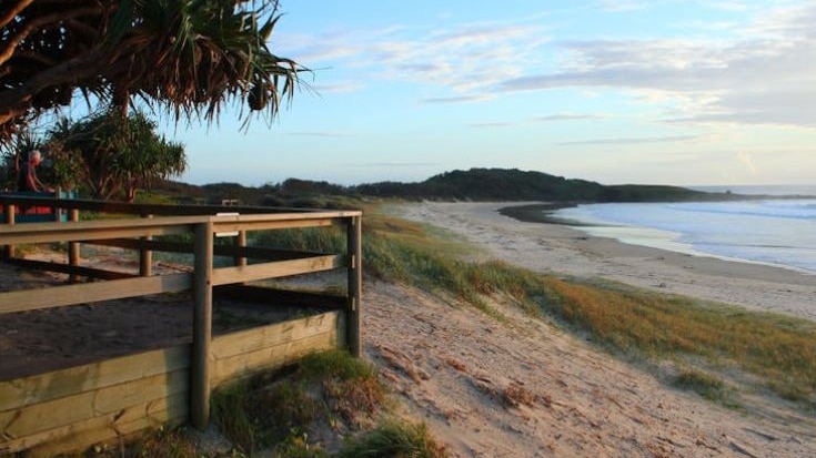 A sandy beach with a wooden viewing deck in the foreground and a headland in the background.