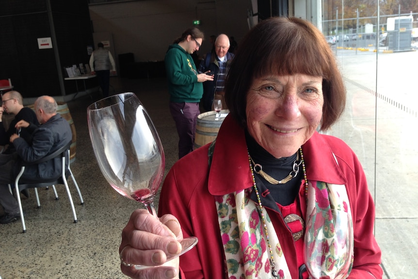 A smiling old white woman with brown hair holding a wine glass