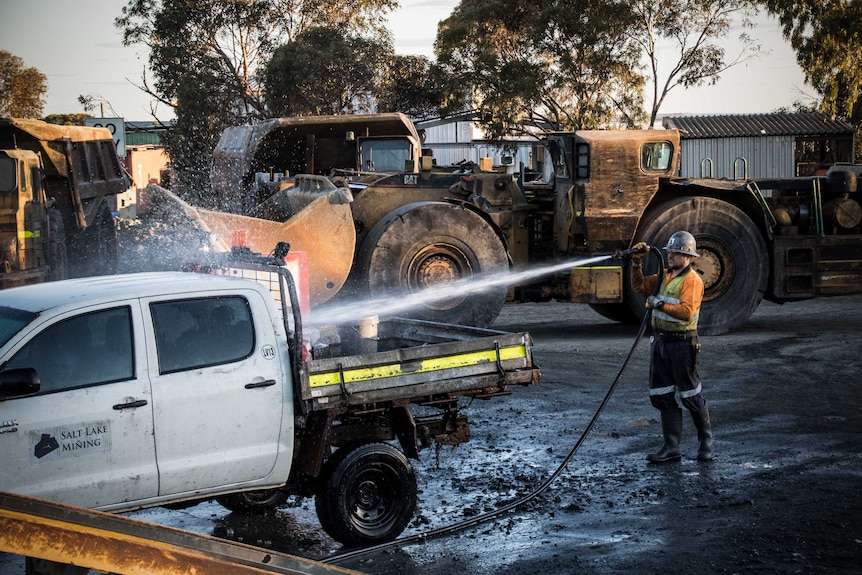 Worker cleaning vehicle on mine site.