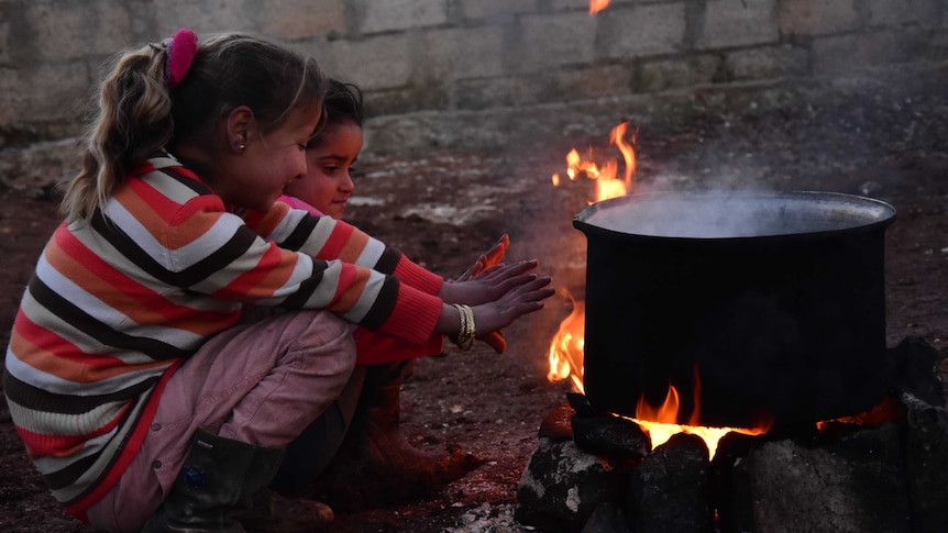 Two children warm themselves by a fire
