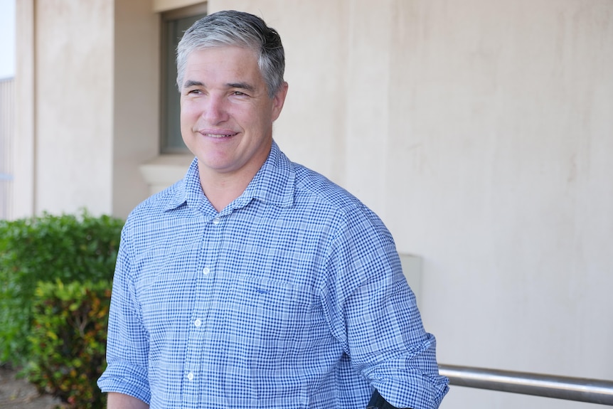 A greying man in a blue button up smiles.