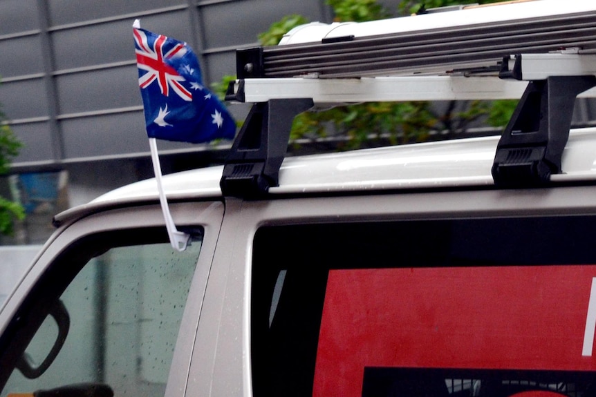 An Australian flag attached to the window of a van flutters in the wind.