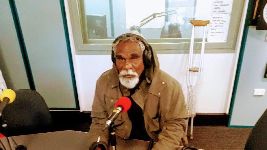 Ned Hargraves sits in a brown jacket talking into a red microphone