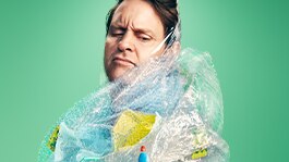 Craig Reucassel, host of war on waste, covered in plastic on an aqua background